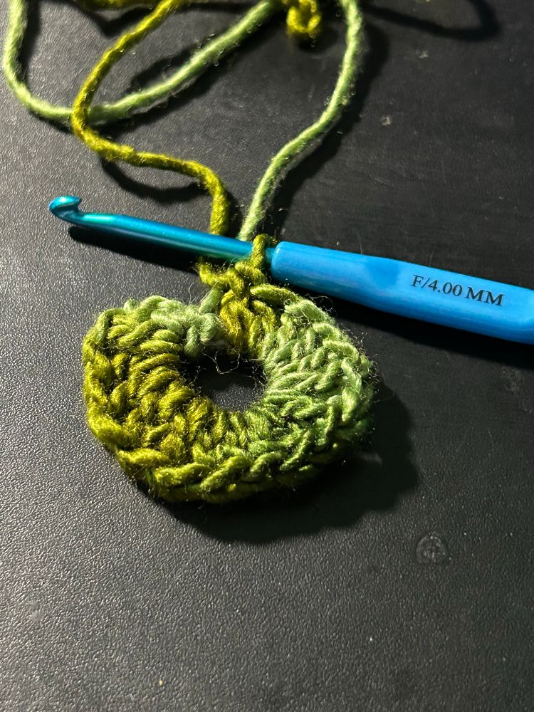Gradient green yarn being crocheted into a green magic circle on a 4.00mm crochet hook.