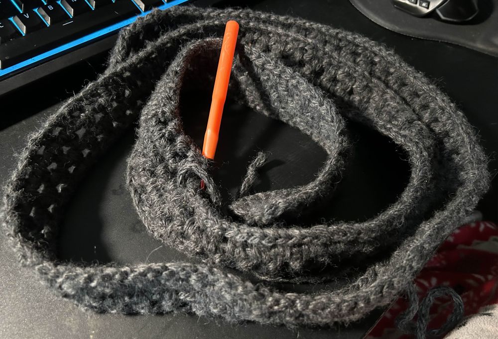 An orange 5.0 crochet hook resting in a coiled up on a crochet belt.