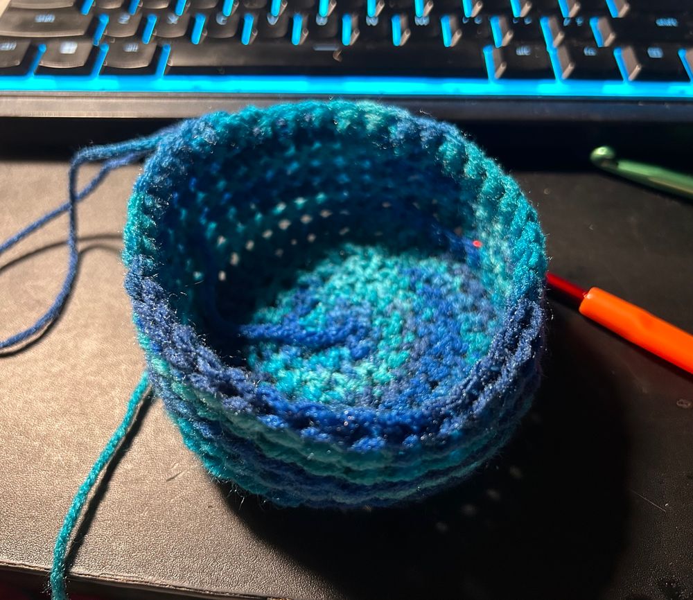 A blue gradient crochet bowl that came from the attempt of a magic circle. There is a 5.0mm and a 7.0mm hook next to the bowl and a keyboard behind it.