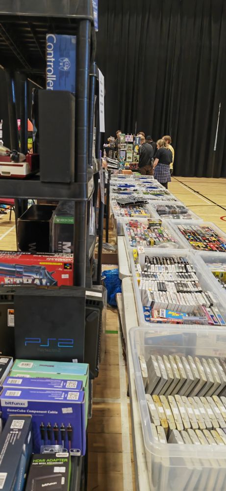 A photograph of a shelf containing old video game consoles. To the right after lots of old games in white plastic containers.