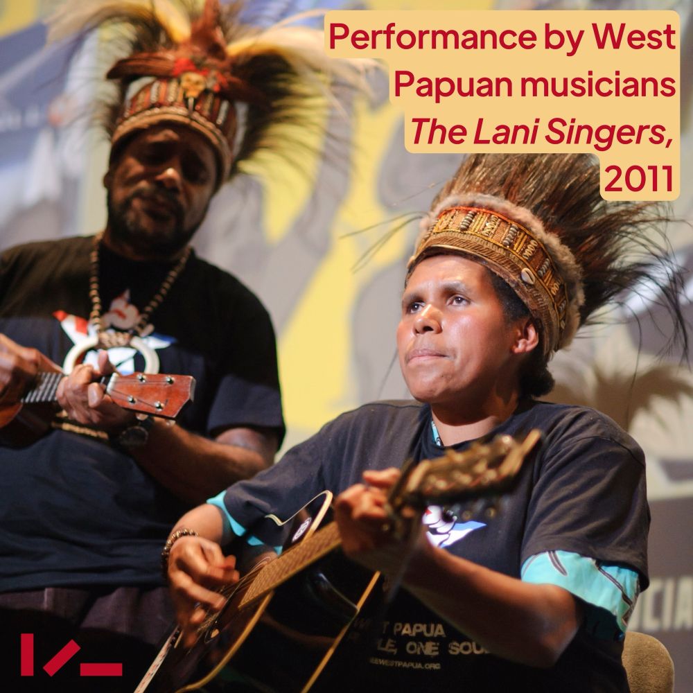 Photograph of two people wearing headdresses adorned with feathers, fabric and cowrie shells. One is seated and plays a guitar. The other is standing and plays a ukelele. Overlayed text reads: Performance by West Papuan musicians, The Lani Singers, 2011.