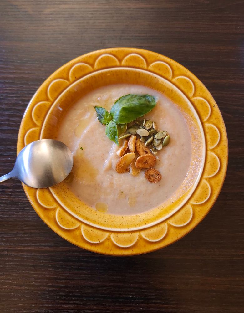A floral mustard colored bowl containing cauliflower soup. Garnished with garlic pepitas and basil sprig. The drizzled oil is infused with basil but doesnt appear green. Recipe by Glamorosi!