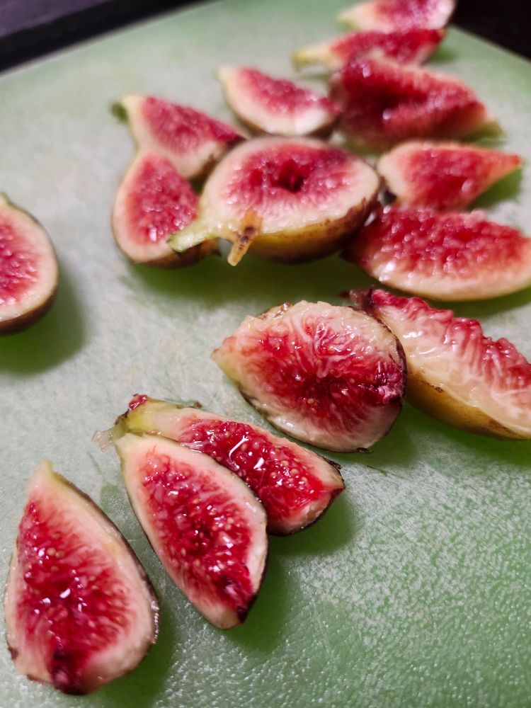 Fresh brown figs with bright red centers roughly chopped and scattered on a green cutting board. They are beautiful but slightly grotesque. 