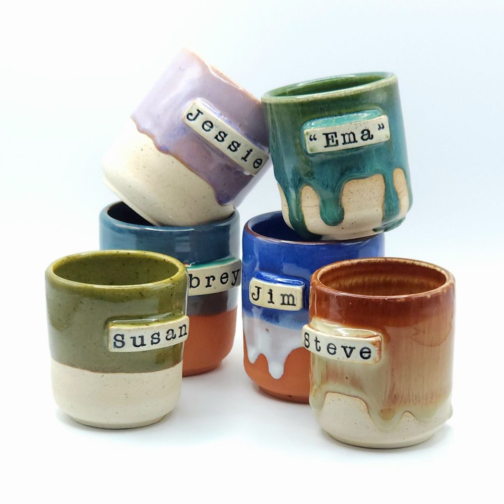 A collection of differently colored ceramic cups, customized with different people's names.