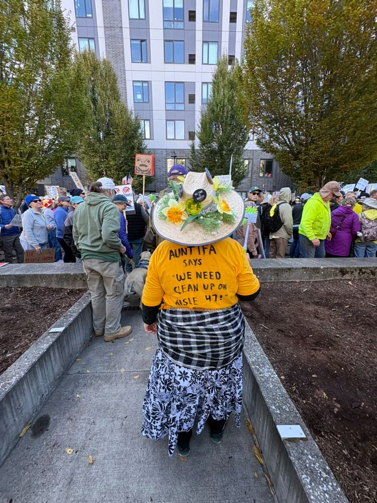Protestor's shirt reads "Antida says "we need clean up on aisle 47" written in black marker on a bright yellow shirt.