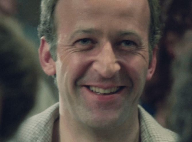 ChatGPT describes the image as "The image shows a middle-aged man with a broad, genuine smile, exuding warmth and friendliness. He has short, light-colored hair and wears a checkered shirt, suggesting a casual or semi-casual setting. The background is blurred but indicates an indoor environment, possibly a social or informal gathering. The man's expression hints at a moment of shared amusement or happiness, and his eyes convey a sense of kindness and sincerity. In the context of the series, this scene likely captures a pivotal or emotionally resonant moment, involving personal connection or revelation. The atmosphere appears intimate yet lively, highlighting the character's approachable personality."

BotOfDarkness, version 2.0.23. AWS Lambda version: 1.14.