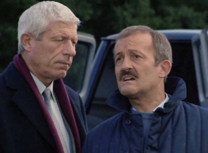 ChatGPT describes the image as "The image depicts two men engaged in a serious conversation outdoors, near a vehicle with an open door. The man on the left has white hair, a solemn expression, and is dressed in a dark coat with a white shirt and a maroon scarf. The man on the right, with graying hair and a mustache, looks distressed and is wearing a blue jacket. The background shows greenery, suggesting a rural or forested setting. The scene conveys a moment of tension or confrontation, possibly involving a critical or emotional revelation, set against a backdrop of seriousness and concern."

BotOfDarkness, version 2.0.23. AWS Lambda version: 1.14.