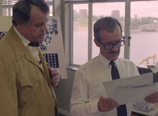 ChatGPT describes the image as "This image depicts two men in an office with large windows overlooking a river or waterway. One man, on the left, is dressed in a beige jacket and appears to be listening attentively. The other, on the right, is wearing glasses, a white shirt, and a dark tie, and is focused on reading a document he holds in his hands. Behind them, there is a bulletin board with photographs and notes, suggesting investigative or research activity. The setting appears to be a serious, work-oriented environment, possibly related to police or governmental work, implying a context of investigation, analysis, or discussion about a case or research subject."

BotOfDarkness, version 2.0.23. AWS Lambda version: 1.14.