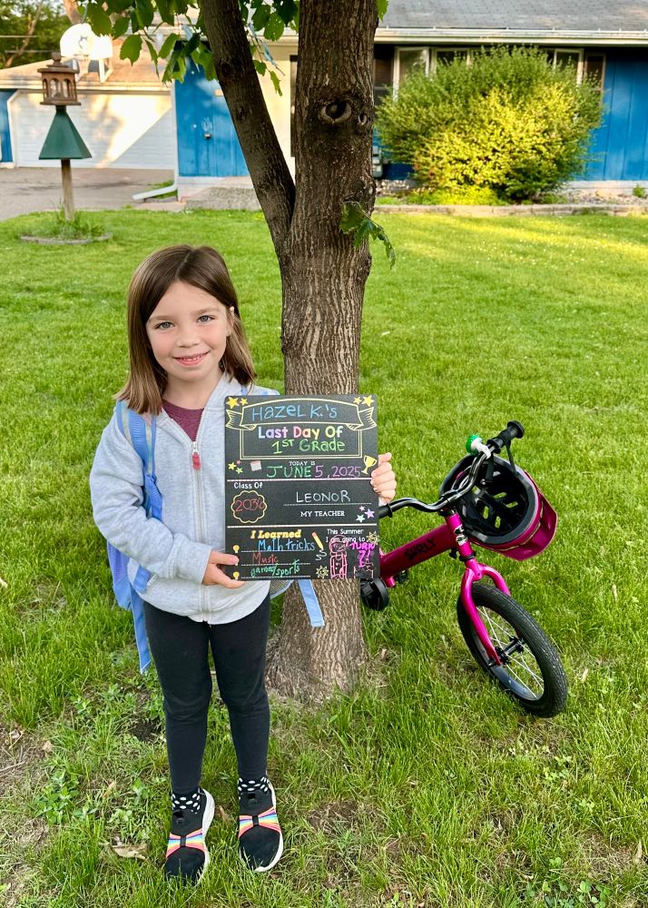 Hazel stands in the front yard next to her pink bike on the last day of first grade