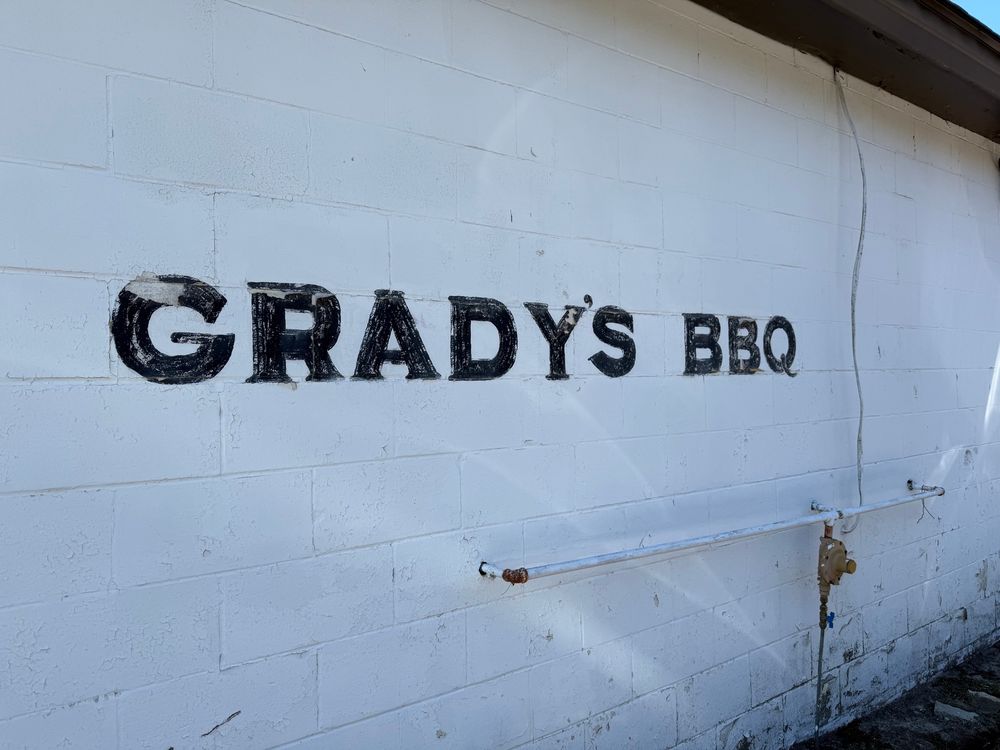 A white brick wall with a hand painted sign in a bold, black copperplate font that reads: GRADY’S BBQ