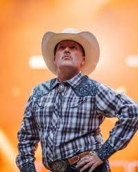 Fred Durst inexplicably dressed in a Western Style shirt with a bolo tie and a cowboy hat picture is taken from below and he has his hand sassily on his hip