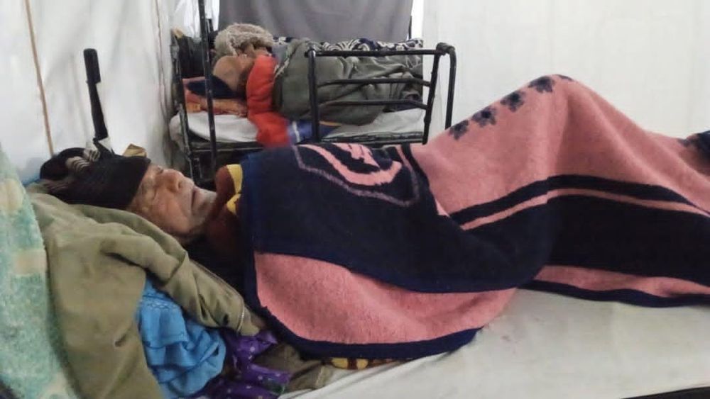An elderly man sleeping on a cot in a
Makeshift hospital 