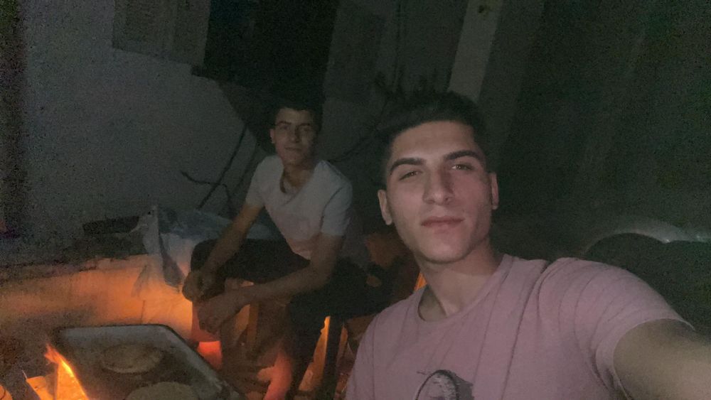 Karam and another young man, they appear to be using a makeshift wood fire 