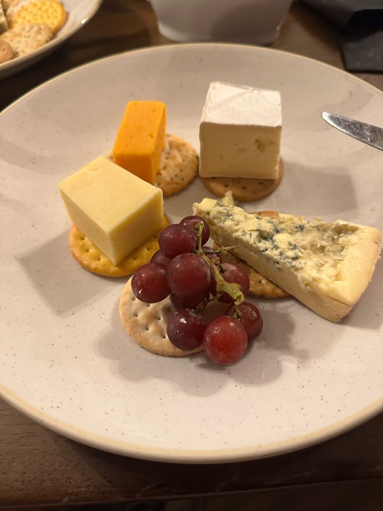 Large bits of cheese sitting on small biscuits. One biscuit is covered by grapes.