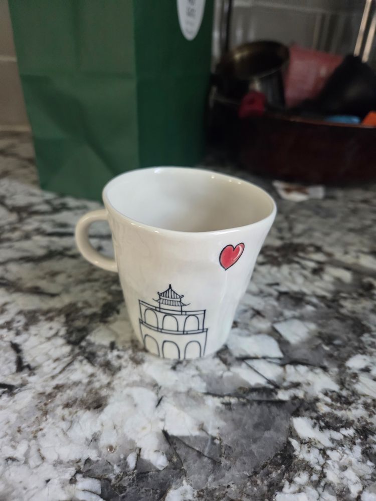 Small white ceramic cup with tiny handle. Image of the Ngoc Son temple with a red love heart in the upper right corner.