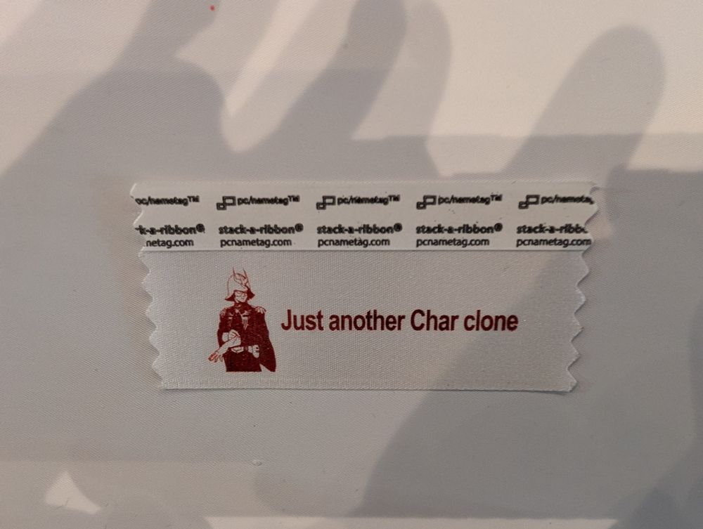 A con badge ribbon with a portrait of Char Aznable and text that reads "Just another Char clone"