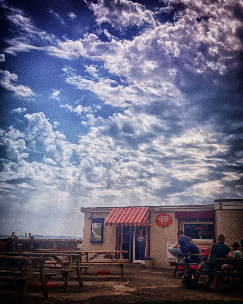 The beach café at Llantwit Major with a cloudy sky and sun rays.