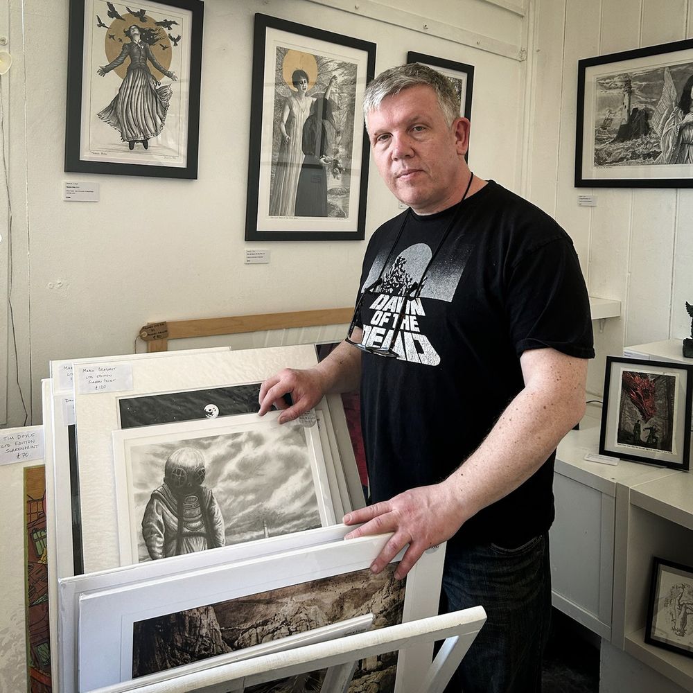 Photograph of Welsh artist David W. J. Lloyd looking through the print browser in a gallery filled with his work
