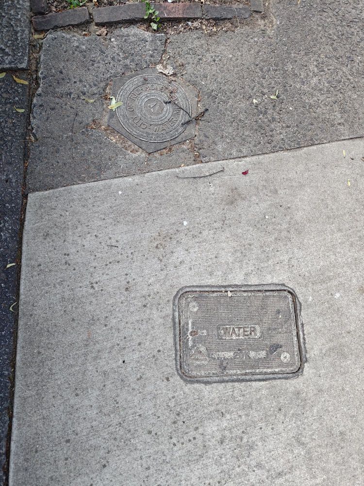 A photo of 2 water meter covers. The lower one is a plastic rectangle, the upper one is a plastic circle.