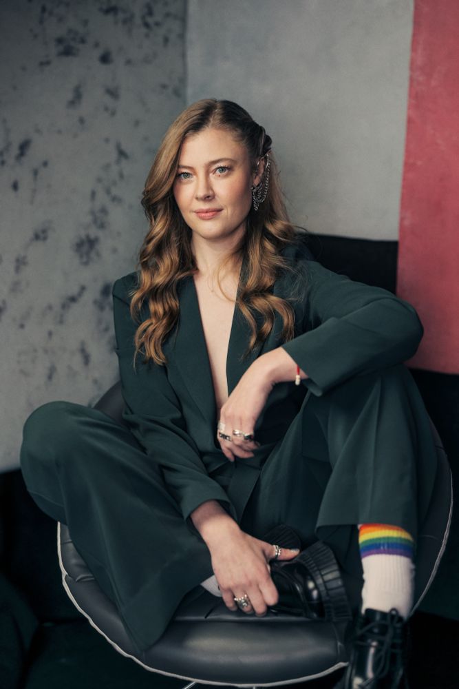 jennifer english poses on a chair, sitting the gay way, exposing her rainbow coloured socks she’s wearing under her forest green suit. 

ps. no shirt or blouse is worn under the suit, it’s very hot. 