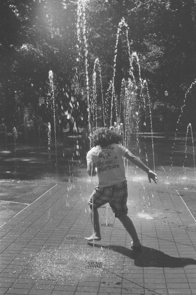A black and white photo of a teenager running through a splash pad. 