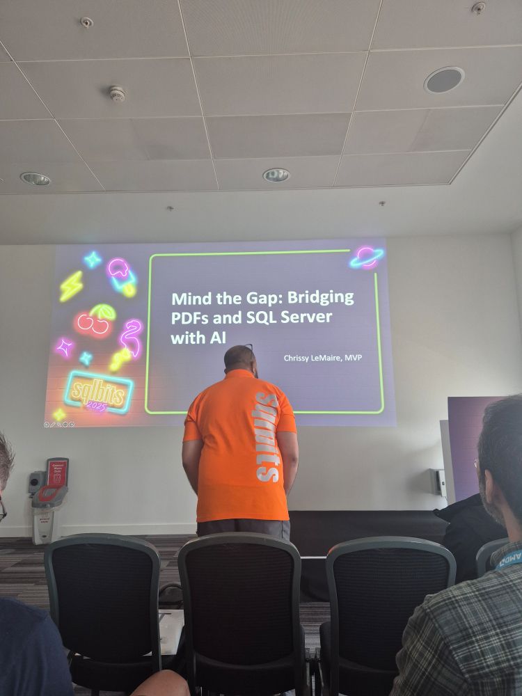 A volunteer with sqlbits on the back of his shirt in front of a slide with the title of the talk