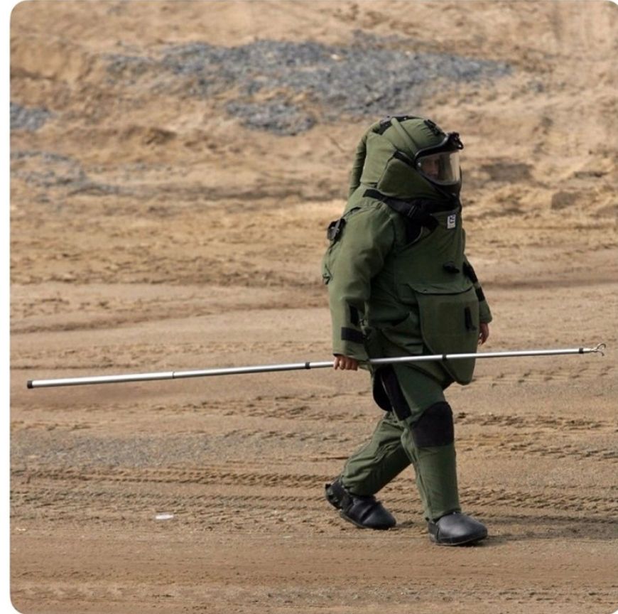 Bomb disposal operative fully suited up in gear with a big stick to explode bombs...