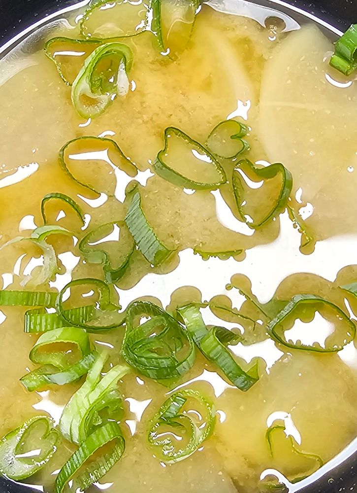 Slices of green onion in miso soup with slices of white radish.