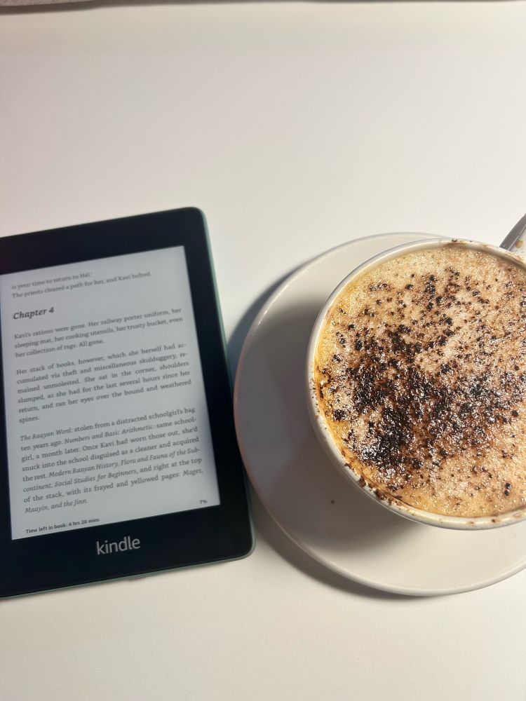 A kindle next to a cup of coffee.