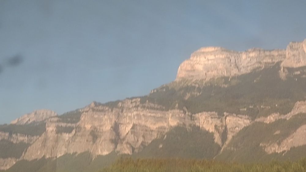 Photo de mauvaise qualité, prise depuis un train aux vitres sales, montrant une partie des falaises du massif de la Chartreuse surplombant le Grésivaudan, avec en particulier la Dent de Crolles.