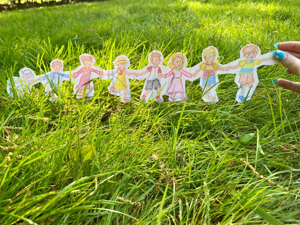 a cutout crayon drawing of all the children of tazmily, pre-timeskip. the cutout is being held on my front lawn to make it look like they’re running through the grass, because i realized i wouldn’t have time to actually draw a background