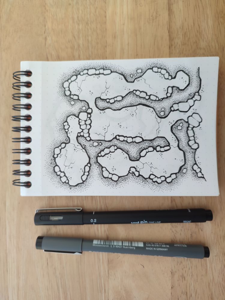 A top down cave map drawn in a small drawing pad, along with the pens used.