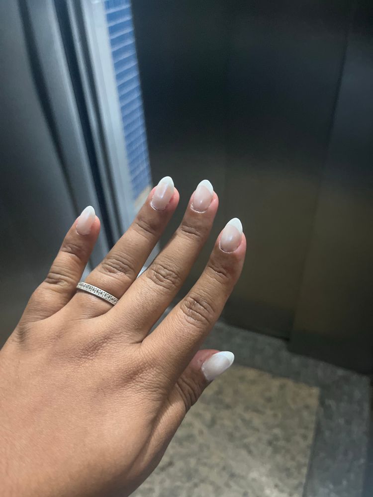 Foto de mão negra com meia aliança prata com brilhante no dedo anelas e unhas grandes e pontudas em todos os dedos. Estou dentro de um elevador. 