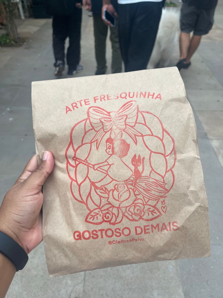 Embalagem de papel com estampa da Kiki (filme do estúdio Ghibli) com os dizeres “arte fresquinha gostoso demais”. 