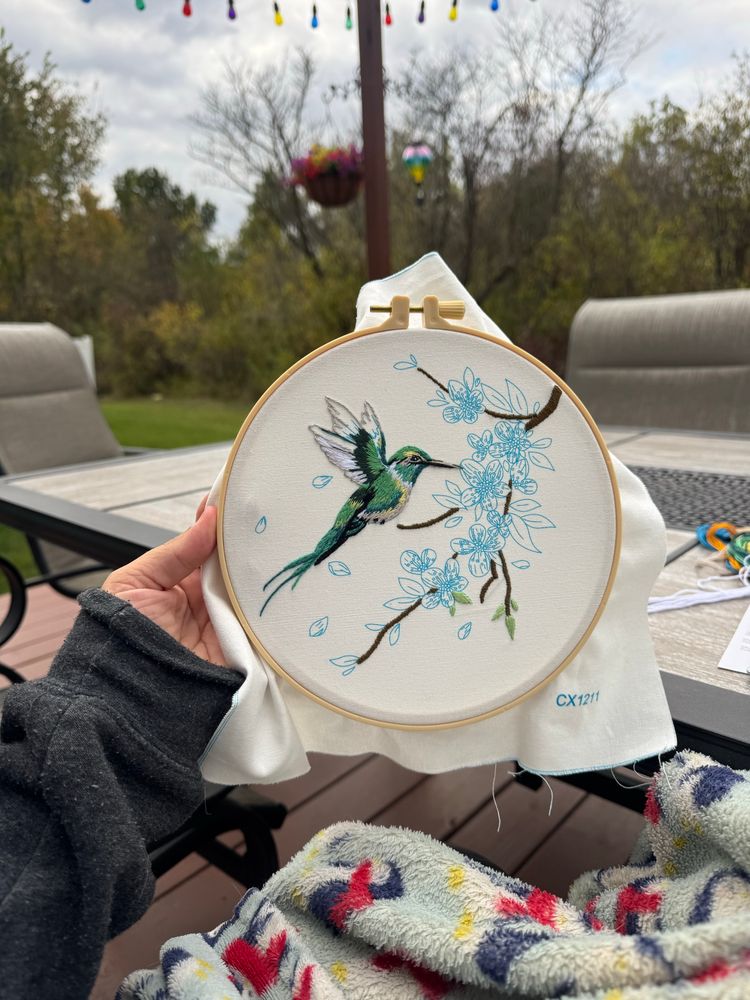 A photo of me holding an embroidery circle with a hummingbird on it. It’s green and yellow. 