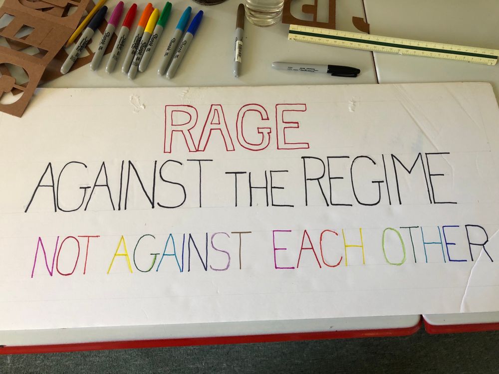 Hand lettered poster: RAGE [in red] against the regime [in black] not against each other [rainbow]