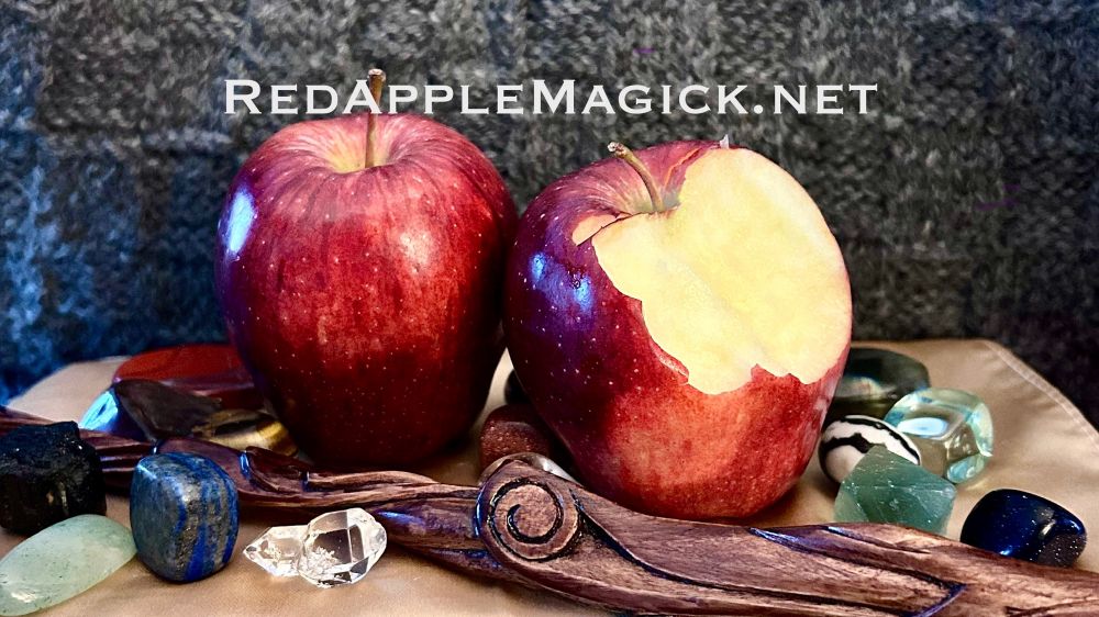 A banner photo of 2 red soles, one with a bite taken out, with some polished crystals and a wand against a grey background with the text added, “RedAppleMagick.net”
