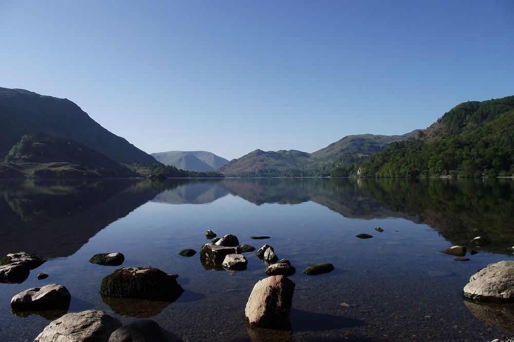 Reflections on Ullswater, the Lake District, Cumbria, UK of fells either side of the photo and a pale blue sky,