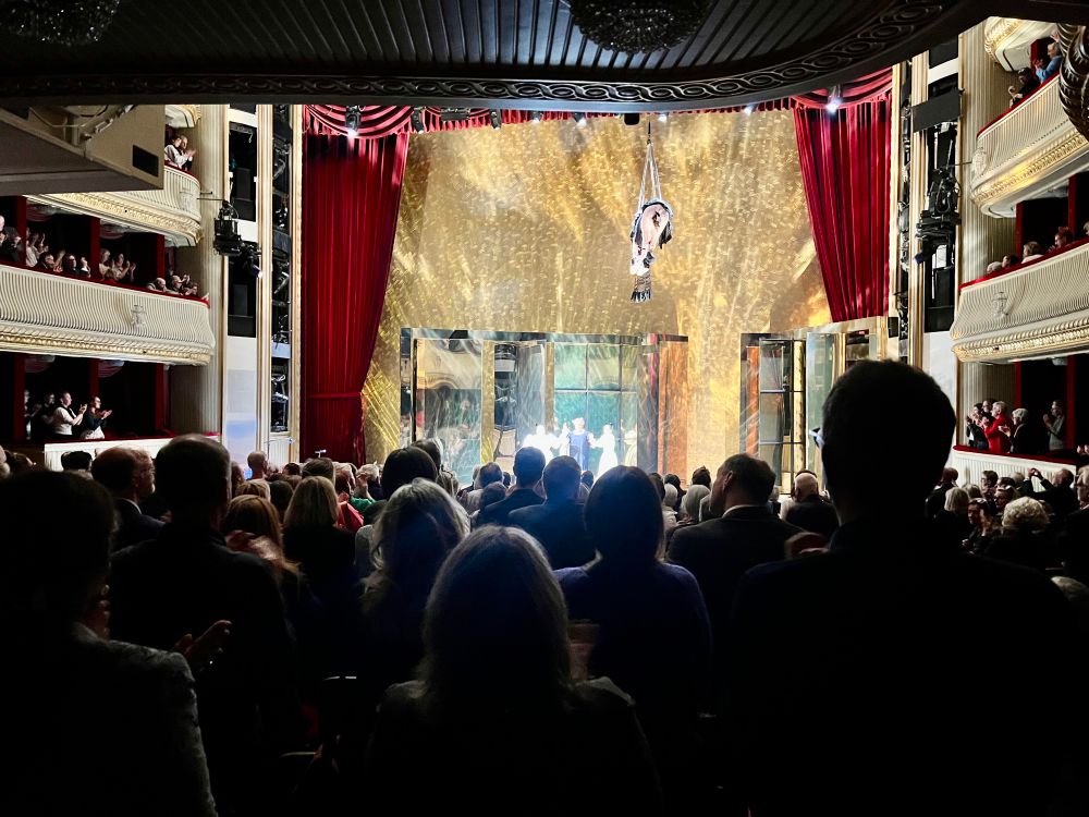 Das Publikum im Burgtheater von hinten, es steht und applaudiert. Auf der Bühne die Schauspielerin Stefanie Reinsperger mit den zwei Musikerinnen Lilian Kaufmann und Elena Ulrich