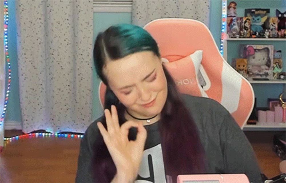 a woman with blue hair is giving an ok sign in front of a pink chair