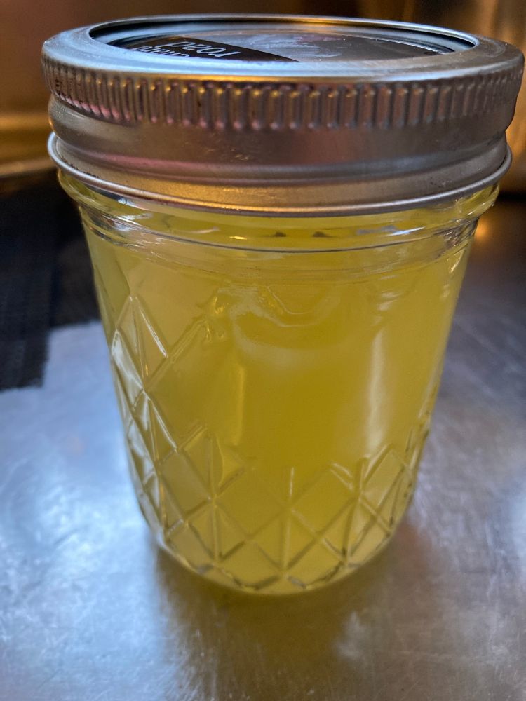 A 250ml capacity glass jar filled with lemon syrup. It is on a stainless steel kitchen bench, and has a lid held on with a screw band.
