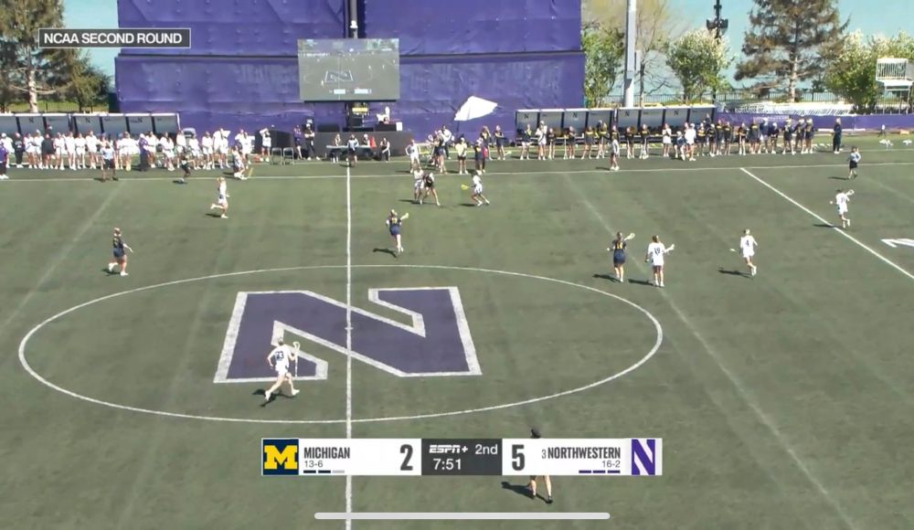 Northwestern’s lacrosse stadium, by a lake. There is a video board at midfield, showing a live feed of the game. So the screen is showing a tiny version of Northwestern’s lacrosse stadium with a tiny version of the screen, presumably displaying an even tinier image of the stadium and an even tinier version of the screen 