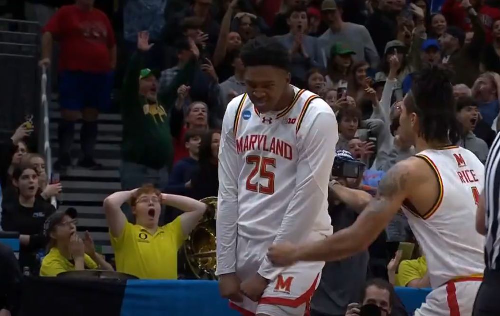Derik Queen flexes his muscles after hitting a game-winning shot for Maryland. in the background, a red-headed, glasses-wearing member of the Oregon band wearing a bright yellow polo holds his hands on his head, his mouth agape in sheer shock. like the 😮😮😮😮 emoji 