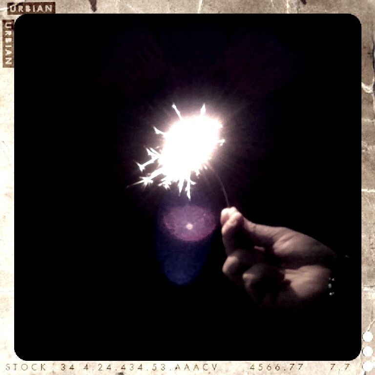 Eine Hand hält eine Wunderkerze vor schwarzem Hintergrund, Bild in reduzierten Farben