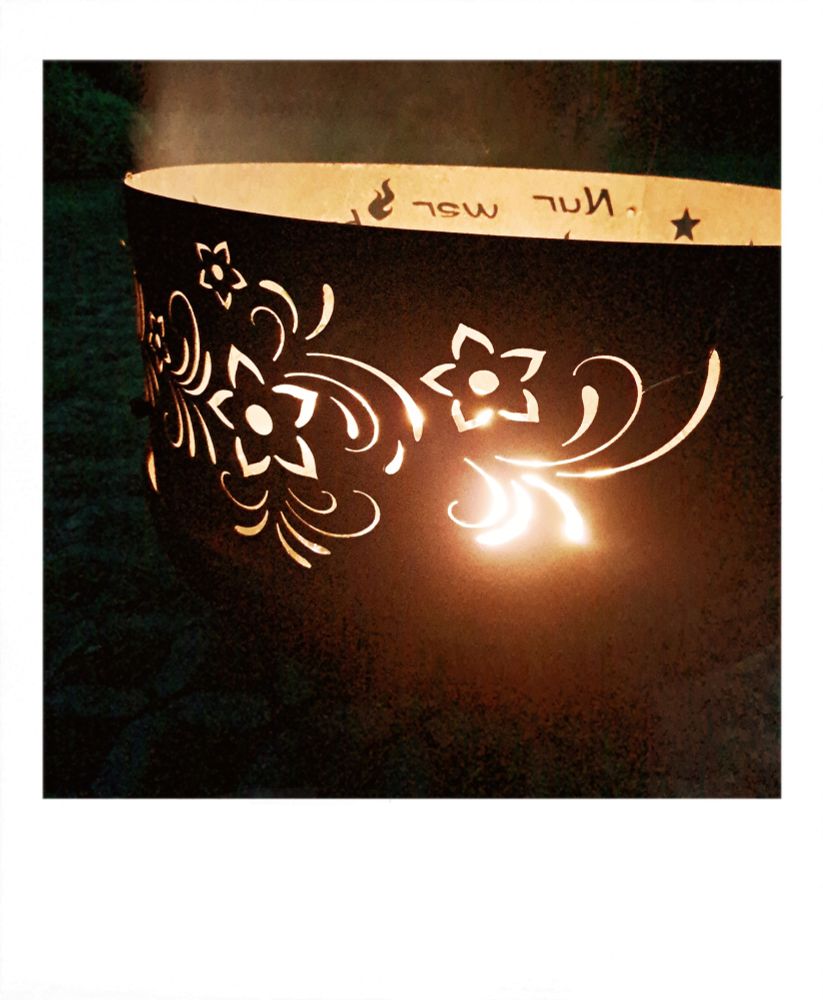 Feuerschale mit einem floralen durchsichtigen Muster am Rand. Dadurch leuchtet das Feuer in der Schale. 