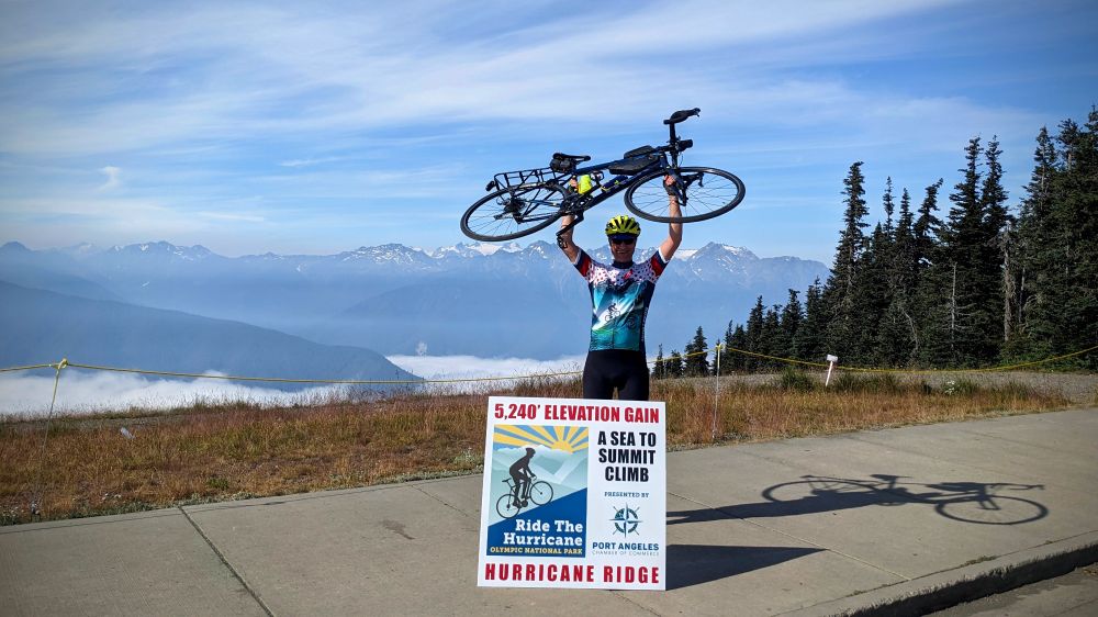 A person holding his bike celebrating. Mountains and valley clouds in the background