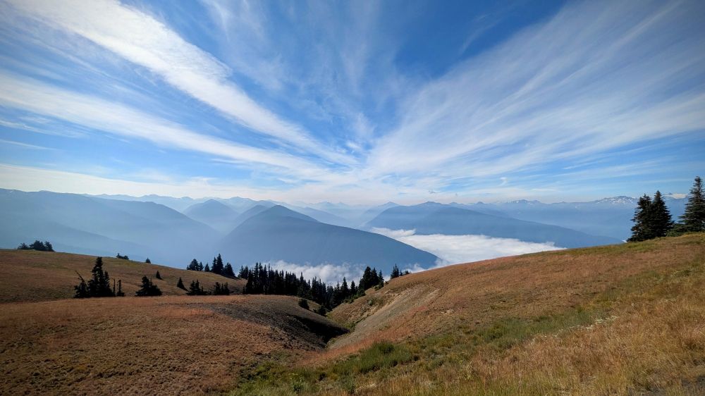 Dry hills, mountains in the distance, clouds blanketing the valley with wisps of clouds high in the sky.