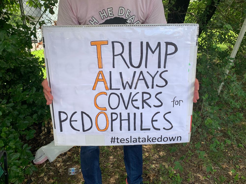 A sign that says, “TACO - Trump Always Covers for Pedophiles,” with the ‘O’ in Pedophiles highlighted. 
