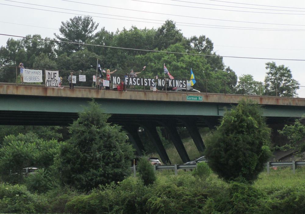 Group of protesters on an overpass with a large sign that says, “No Fascists No Kings.” 