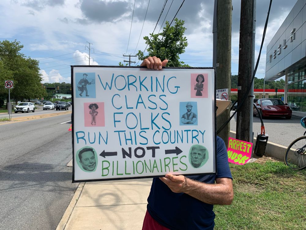 A protester holding a sign that says, “Working Class Folks Run This Country NOT Billionaires.” 